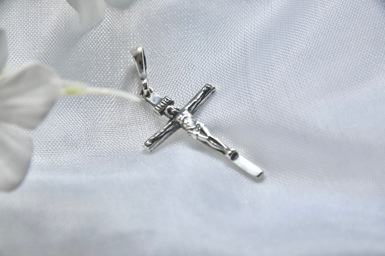 Puede incluir: Un colgante de plata en forma de cruz con una figura detallada de Jesucristo. El colgante est&aacute; sobre un fondo de tela blanca.