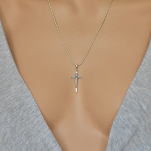 Puede incluir: Un collar de cadena de plata con un colgante de crucifijo de plata.