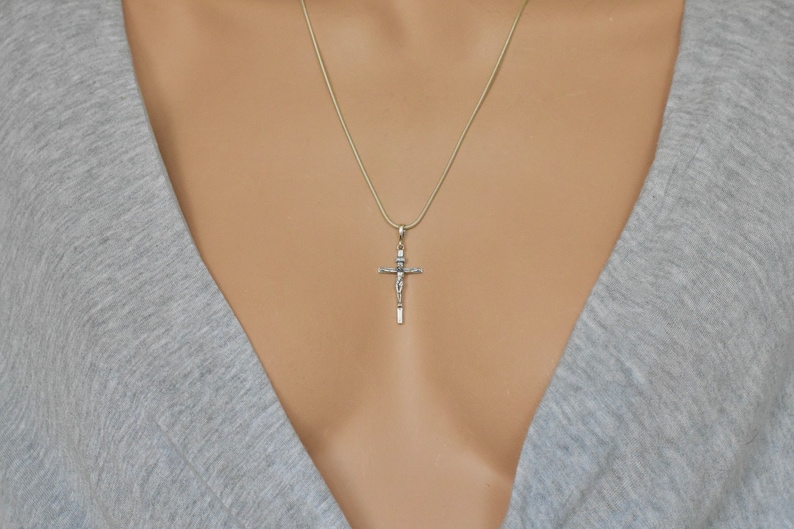 Puede incluir: Un collar de cadena de plata con un colgante de crucifijo de plata.