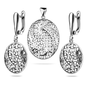 May include: A silver pendant and earrings set with an intricate floral design. The pendant and earrings are oval shaped and feature a delicate filigree pattern.
