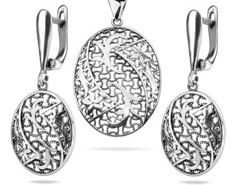 May include: A silver pendant and earrings set with an intricate floral design. The pendant and earrings are oval shaped and feature a delicate filigree pattern.