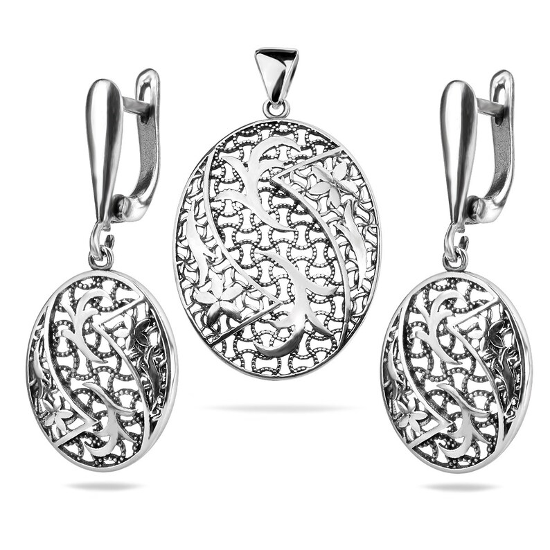 May include: A silver pendant and earrings set with an intricate floral design. The pendant and earrings are oval shaped and feature a delicate filigree pattern.