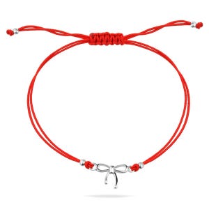 Puede incluir: Un brazalete de cuerda roja con un dije de plata en forma de lazo. El brazalete es ajustable y tiene un diseño simple.