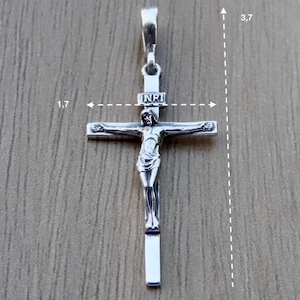 Puede incluir: Pendiente de plata en forma de cruz con una figura de Jesucristo en la cruz. El pendiente mide 4,3 cm de ancho y 9,4 cm de alto. La inscripci&oacute;n "INRI" es visible en la cruz.