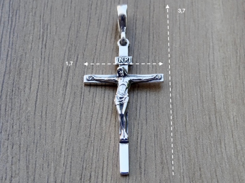 Puede incluir: Pendiente de plata en forma de cruz con una figura de Jesucristo en la cruz. El pendiente mide 4,3 cm de ancho y 9,4 cm de alto. La inscripci&oacute;n "INRI" es visible en la cruz.