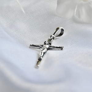 Puede incluir: Pendiente de plata en forma de crucifijo con una figura de Jesucristo en la cruz.
