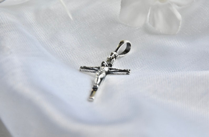 Puede incluir: Pendiente de plata en forma de crucifijo con una figura de Jesucristo en la cruz.