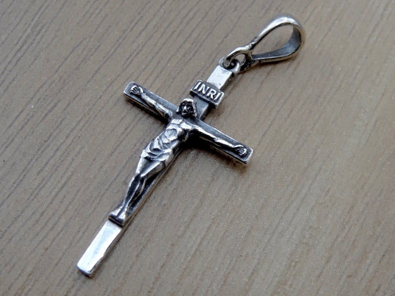 Puede incluir: Pendiente de cruz de plata con una figura detallada de Jesucristo y la inscripci&oacute;n "INRI" en la cruz.