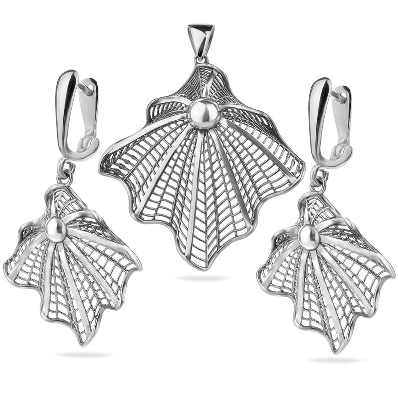 May include: A silver filigree pendant necklace and matching earrings set. The pendant and earrings are shaped like a stylised shell with a delicate, intricate design.