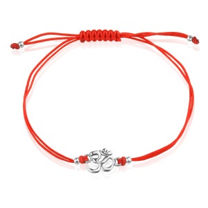 May include: A red string bracelet with a silver Om symbol charm. The bracelet is adjustable and can be tied to fit any wrist.