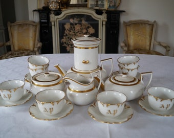 May include: A white porcelain tea set with gold accents. The set includes a teapot, creamer, sugar bowl, and four teacups and saucers. The teacups and saucers have the initials "AP" in gold on the bottom.