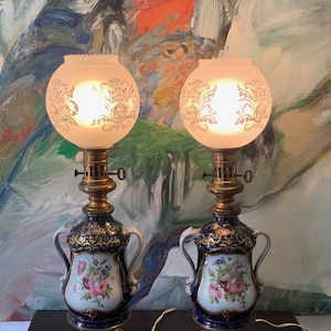 May include: Pair of antique porcelain table lamps with blue and gold accents. The lamps feature floral designs and white frosted glass shades with etched patterns.