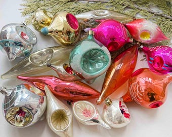 May include: A collection of vintage glass Christmas ornaments in various shapes and colors, including silver, gold, pink, teal, and orange. These reflective baubles feature indented centers, elongated teardrop forms, and delicate painted details.