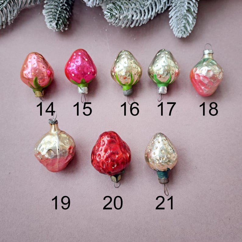 May include: A collection of vintage Christmas ornaments shaped like strawberries and other fruit. The ornaments are in various shades of red, pink, and gold, with green and silver accents. Each ornament has a small metal cap and a loop for hanging. Numbers 14-21 are visible.