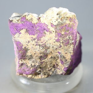 May include: A rough, irregular shaped rock with a purple and silver mineral coating. The rock is about 2 inches tall and 1.5 inches wide.