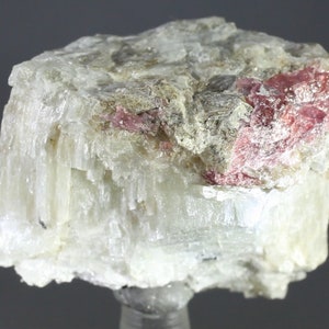 Op de afbeelding: Een cluster van witte, naaldvormige kristallen met een roze mineraal ingebed in het midden.