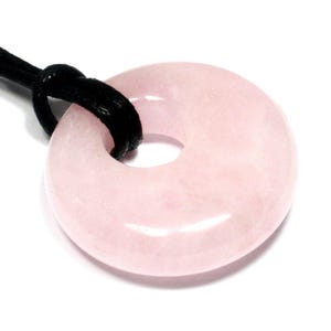 May include: A pale pink rose quartz donut pendant with a black cord. The polished stone has a circular shape with a hole in the centre. The cord is knotted at the top, ready to be worn as a necklace.