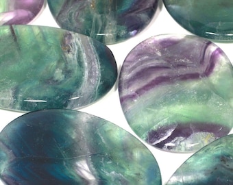 May include: A collection of green, purple, and blue fluorite palm stones. The stones are smooth and polished, with a variety of swirling patterns.