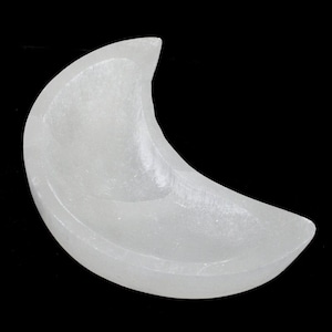 Puede incluir: Un cuenco en forma de media luna tallado en piedra blanca. El cuenco tiene una superficie lisa y pulida y un interior poco profundo. La forma de la luna se destaca sobre un fondo negro. Este artículo decorativo podría usarse para joyas o artículos pequeños.