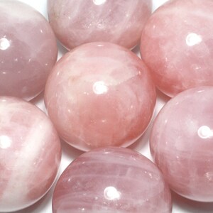 May include: A group of seven smooth, polished rose quartz stones. The stones are a light pink colour and have a glossy finish.
