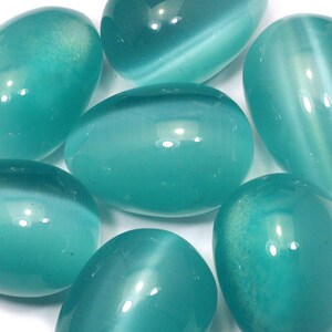 May include: A collection of smooth, oval-shaped teal gemstones. The stones have a polished, glossy surface with subtle internal patterns. The varying sizes and orientations create a visually appealing arrangement, reflecting light and showcasing their natural beauty.