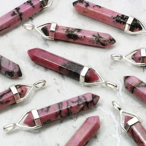 May include: A collection of pink and black gemstone pendants with silver settings. The pendants are in the shape of a point and have a polished finish.