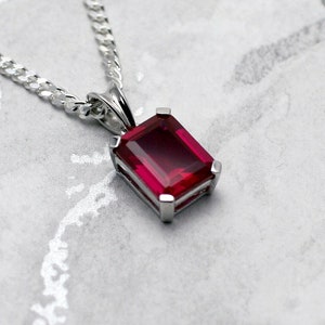 May include: A silver chain necklace with a pendant featuring a large, rectangular, red gemstone.