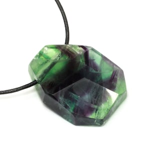 Könnte beinhalten: Ein grüner und violetter Fluorit-Anhänger an einer schwarzen Schnurkette. Der Fluorit ist facettiert und hat eine geometrische Form.