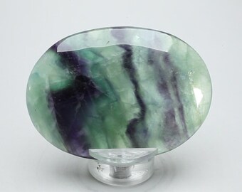 May include: A polished green and purple fluorite oval stone on a clear stand.