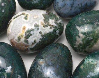 May include: Close-up of several polished gemstones in shades of green, white, and blue. The stones have a smooth, rounded shape and a marbled appearance, with intricate patterns and variations in color. The gemstones are arranged closely together.