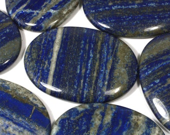 May include: A collection of polished oval-shaped lapis lazuli stones. The stones have a deep blue color with white and gold streaks.