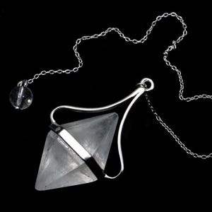 Op de afbeelding: Een zilveren ketting met een slinger van helder kwartskristal. De slinger heeft de vorm van een diamant en hangt aan een zilveren ring.