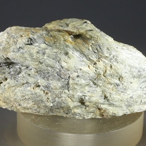 May include: A rough, gray and white rock with a silvery sheen. The rock has a layered, striated texture.
