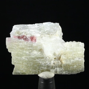 Op de afbeelding: Een cluster van doorschijnende, lichtgroene en witte kristallen met een roze minerale insluiting. De kristallen hebben een gelaagde, gestreepte textuur.