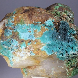 Puede incluir: Un espécimen de roca natural rugoso con una capa de depósitos minerales azul verdoso y verde. La roca tiene una base de cuarzo blanco y transparente.