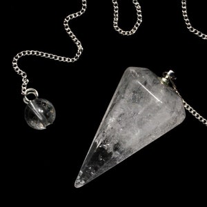 Può includere: Un pendolo di cristallo di quarzo trasparente con una catena d'argento e una piccola perla d'argento. Il pendolo è appeso su uno sfondo nero.