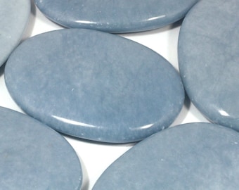 May include: Several smooth, oval-shaped, blue-gray stones are arranged on a white surface. The stones have a polished appearance and a slightly glossy sheen. The color is a muted, cool tone, and the stones appear to be natural.