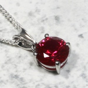 May include: A silver necklace with a red gemstone pendant. The pendant is round and has a faceted design.