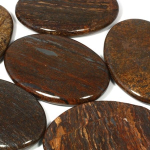 Puede incluir: Cinco piedras lisas pulidas de forma ovalada con un patrón de rayas marrones, rojas y doradas.