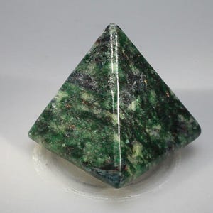May include: A green pyramid-shaped stone with a polished surface. The stone features a mix of dark and light green hues with some black and gold flecks. The pyramid has a smooth, symmetrical design, suitable for home decor or as a collectible item.