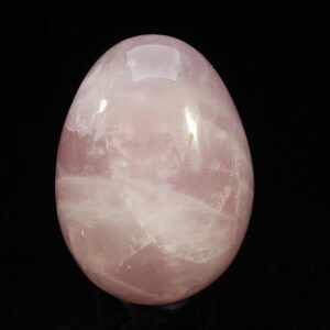 May include: A polished rose quartz egg, displaying a delicate pink colour with faint white streaks. The egg-shaped stone has a smooth, reflective surface, suitable for display or meditation.