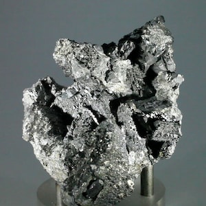 Könnte beinhalten: Ein Cluster aus metallisch grauen, silberfarbenen und schwarzen Kristallen auf einem Ständer. Die Kristalle sind in einer unregelmäßigen, gezackten Form angeordnet.