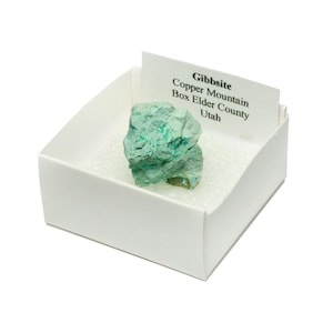 May include: A small, green, rough-textured rock labeled "Gibbsite, Copper Mountain, Box Elder County, Utah" in a white box.