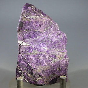 May include: A large, rough, purple and gray rock specimen on a metal stand. The rock has a layered, striated texture.