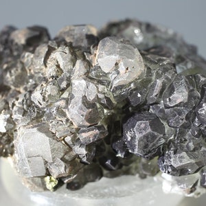 May include: A cluster of gray, metallic, faceted crystals. The crystals are arranged in a random pattern and have a shiny, reflective surface.