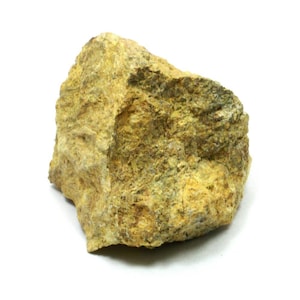 Puede incluir: Una roca rugosa de color amarillo-marrón con una superficie texturizada. La roca tiene un aspecto natural y terroso.