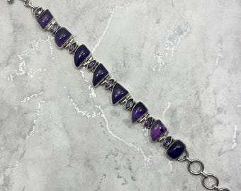 May include: A silver bracelet with a clasp and purple amethyst stones. The stones are faceted and have a geometric shape.