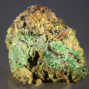 Puede incluir: Primer plano de un espécimen mineral con una superficie rugosa y texturizada. La roca presenta una mezcla de colores, incluyendo verde vibrante, amarillo dorado y tonos marrones terrosos. El mineral parece ser una formación natural.