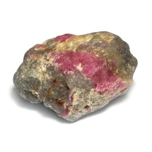 May include: A rough, gray and pink ruby gemstone. The ruby is a natural stone with a rough, unpolished surface.
