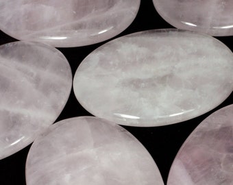 May include: Six smooth, oval-shaped rose quartz stones, each with a light pink hue and subtle striations, are arranged on a black background.